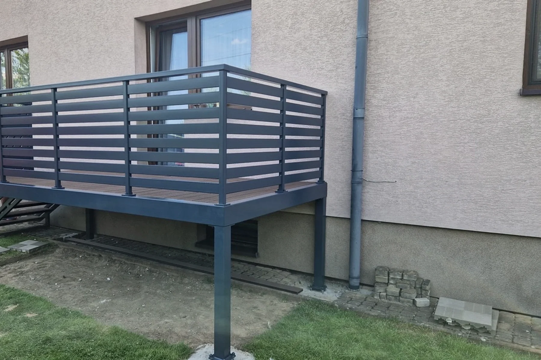 Stalowy podest z balustradą przy elewacji.